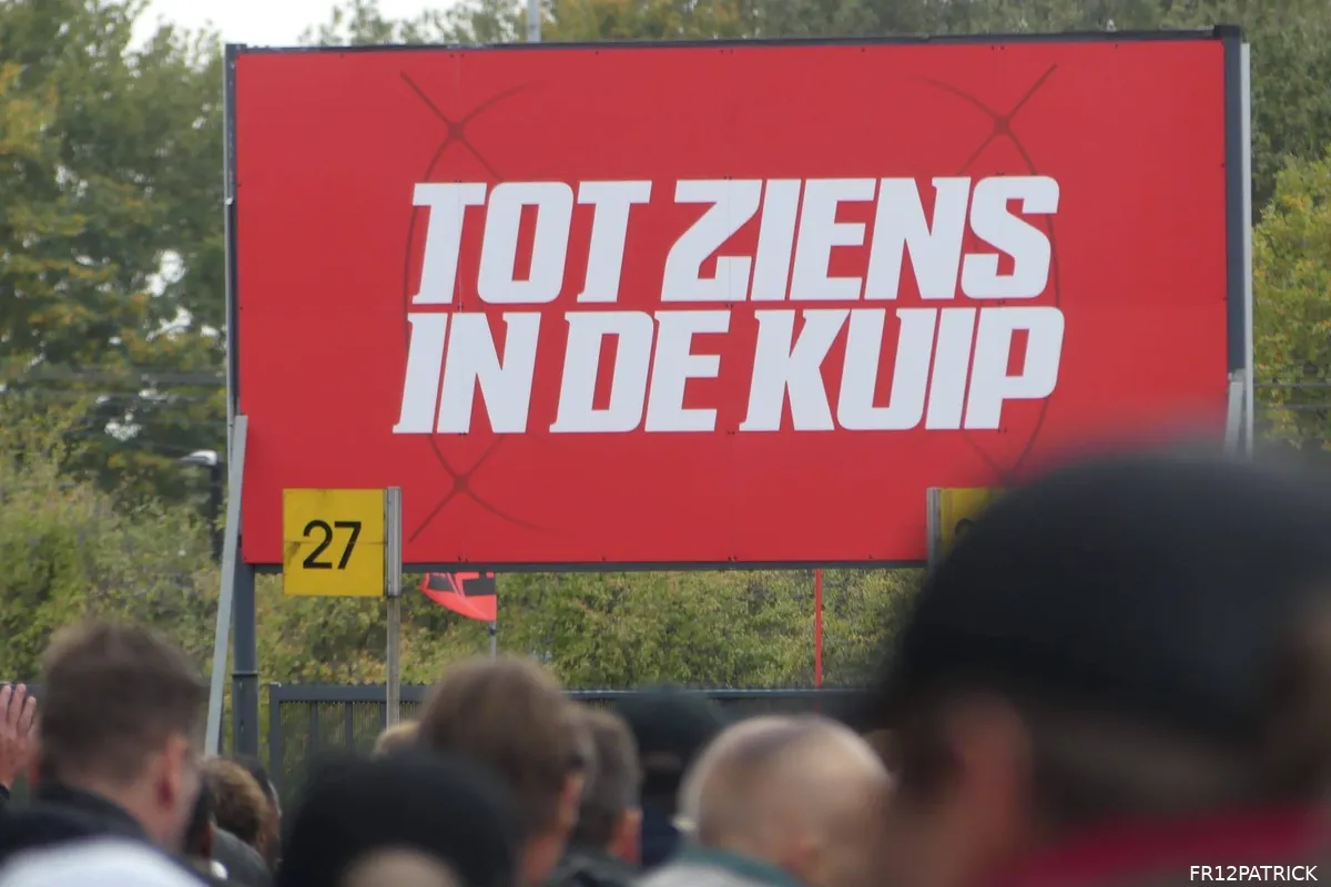 Supporters van Feyenoord lopen richting De Kuip langs een groot bord met de tekst 'Tot ziens in De Kuip' voorafgaand aan een thuiswedstrijd.