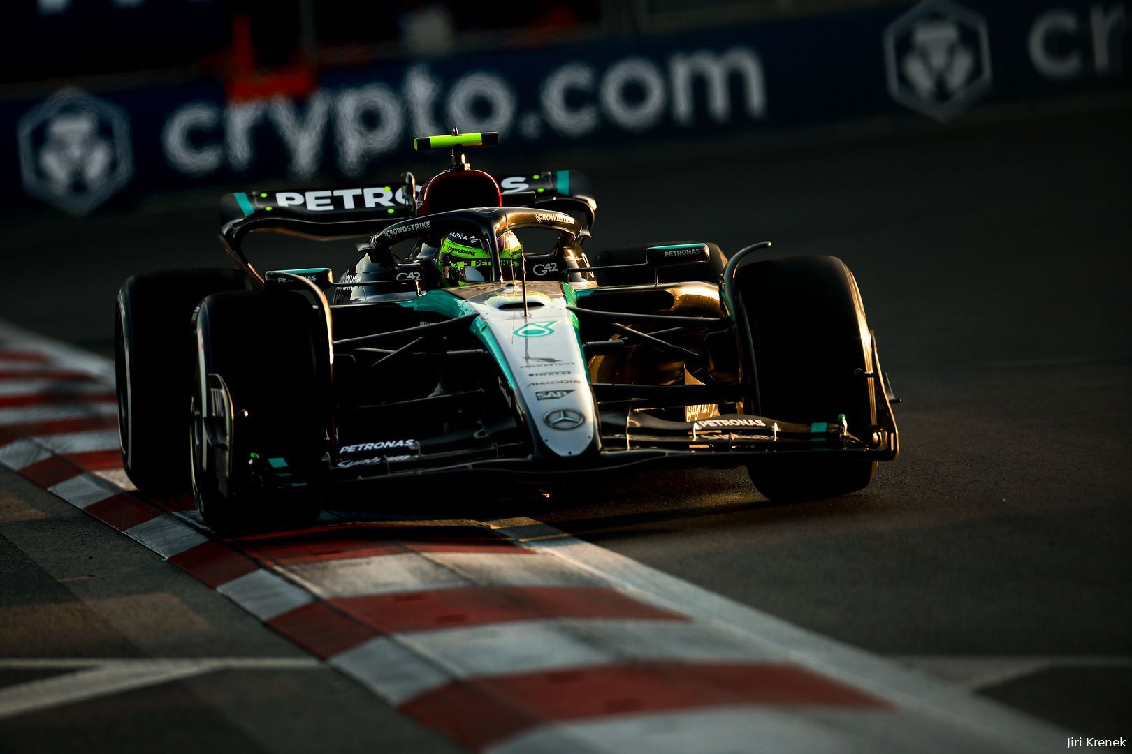 Lewis Hamilton driving his Mercedes over the white and red curb at the Baku City Circuit during golden hour, with advertising banners visible in the background.