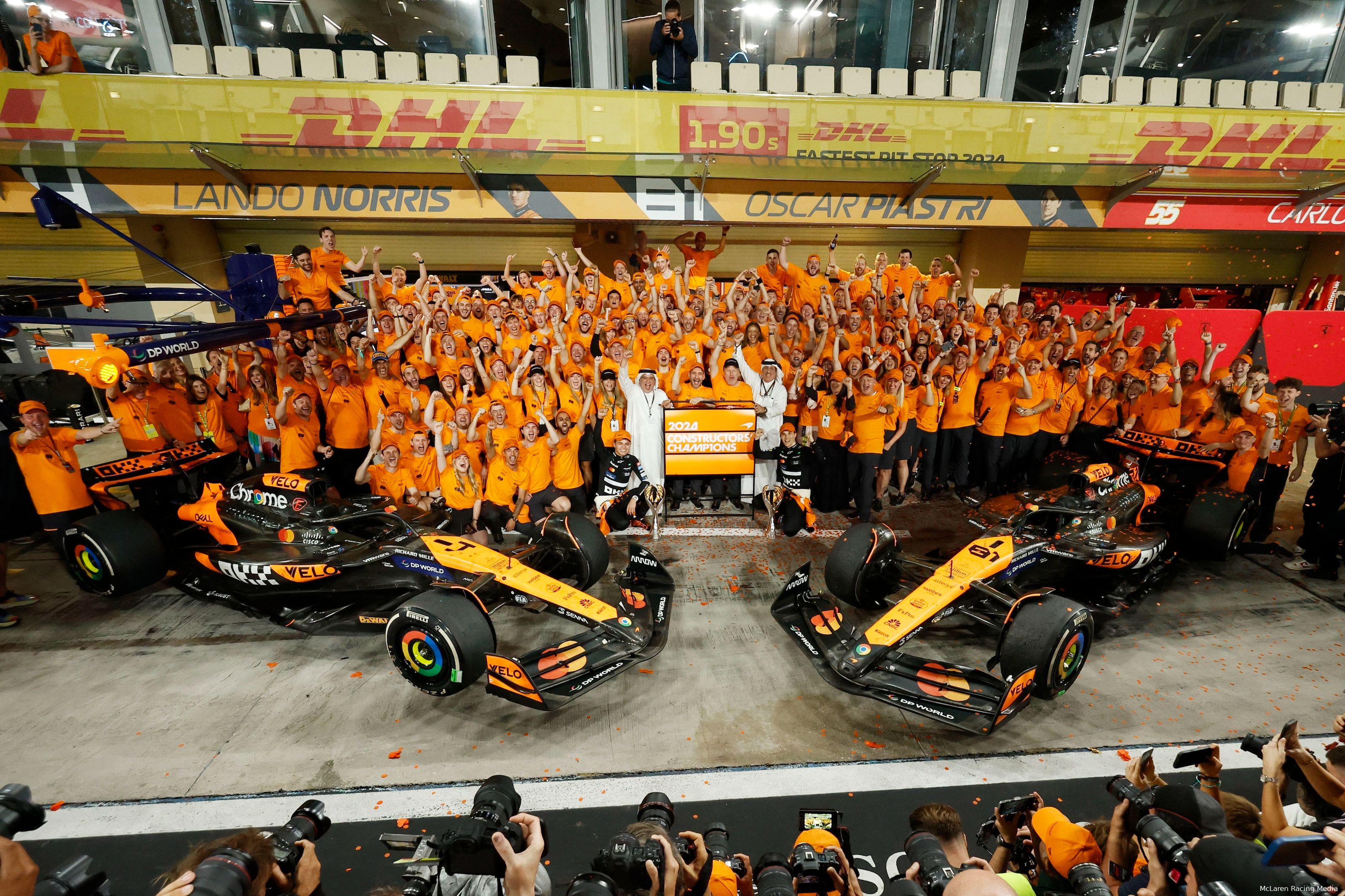 The McLaren Racing team poses for a celebratory photo after securing the 2024 Constructors' title in Abu Dhabi, gathered around both cars in front of their garage.