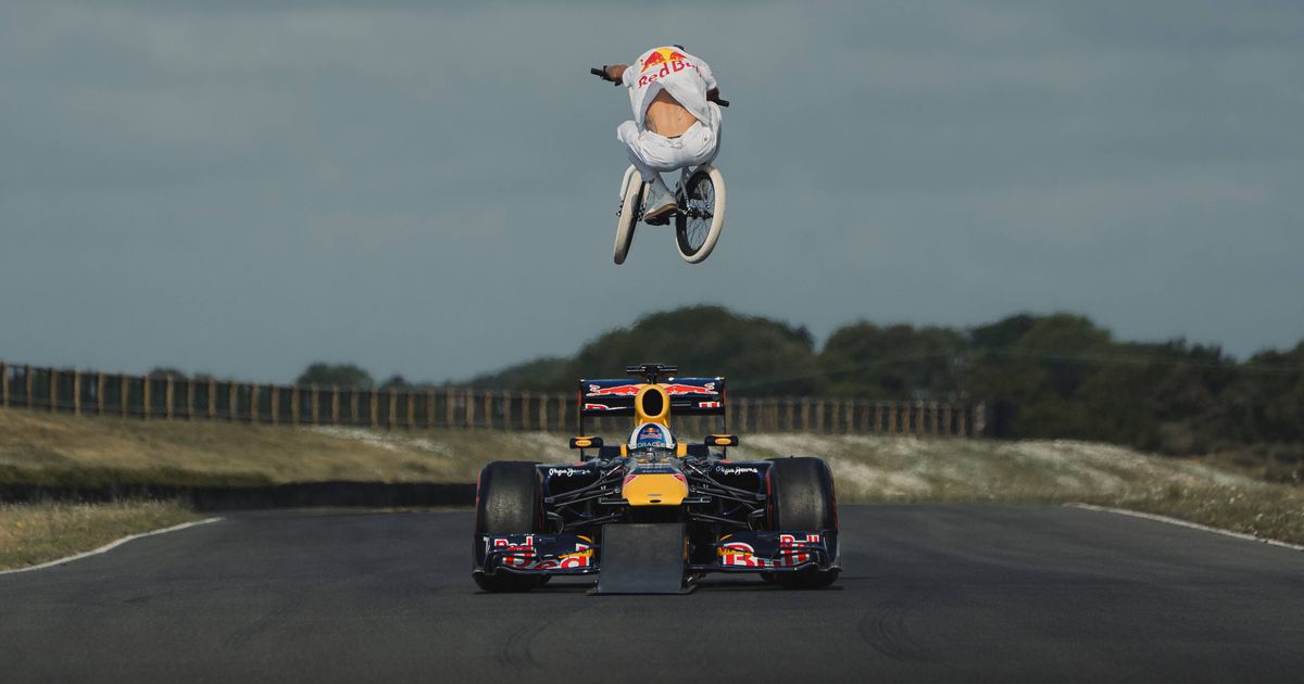 Springendes Renn Auto Met een fiets over een rijdende Red Bull F1-auto springen: Episch of ...