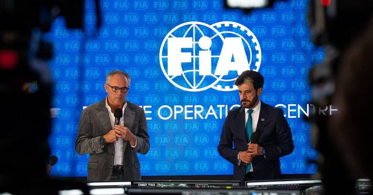Two men holding microphones before a blue FIA-branded backdrop, with monitors in the foreground.