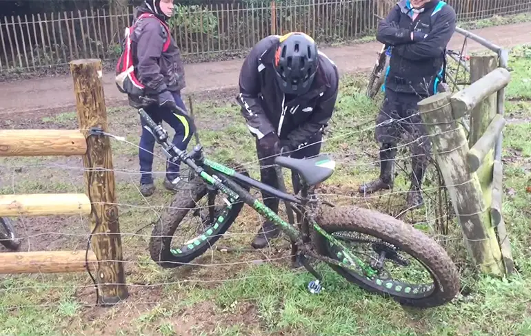 Drie mannen proberen fiets los te maken uit hek met schrikdraad
