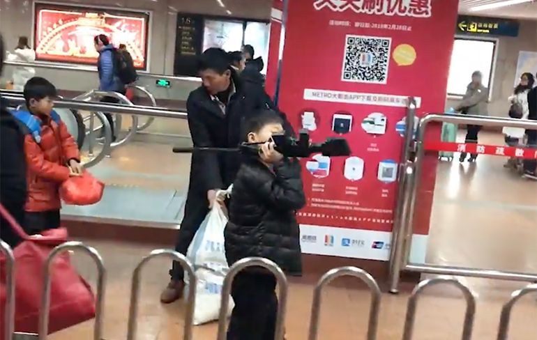 Kind loopt met realistisch ogend speelgoedgeweer door metro Shanghai