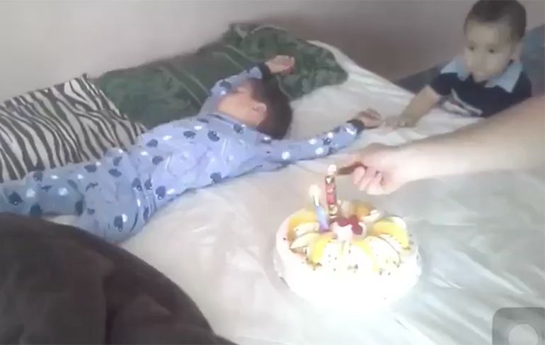 Slaperig kind krijgt taart met kaars en serenade aan bed