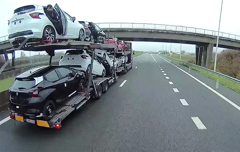 Trucker filmt migranten die meeliften op oplegger vol nieuwe auto's