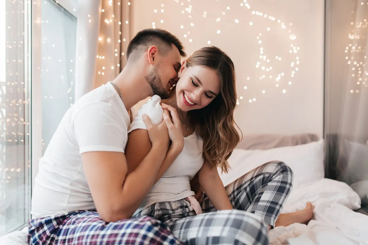 caucasian man checkered pajama kissing his wife smiling blonde woman sleepwear sitting bed with boyfriend 197531 8330