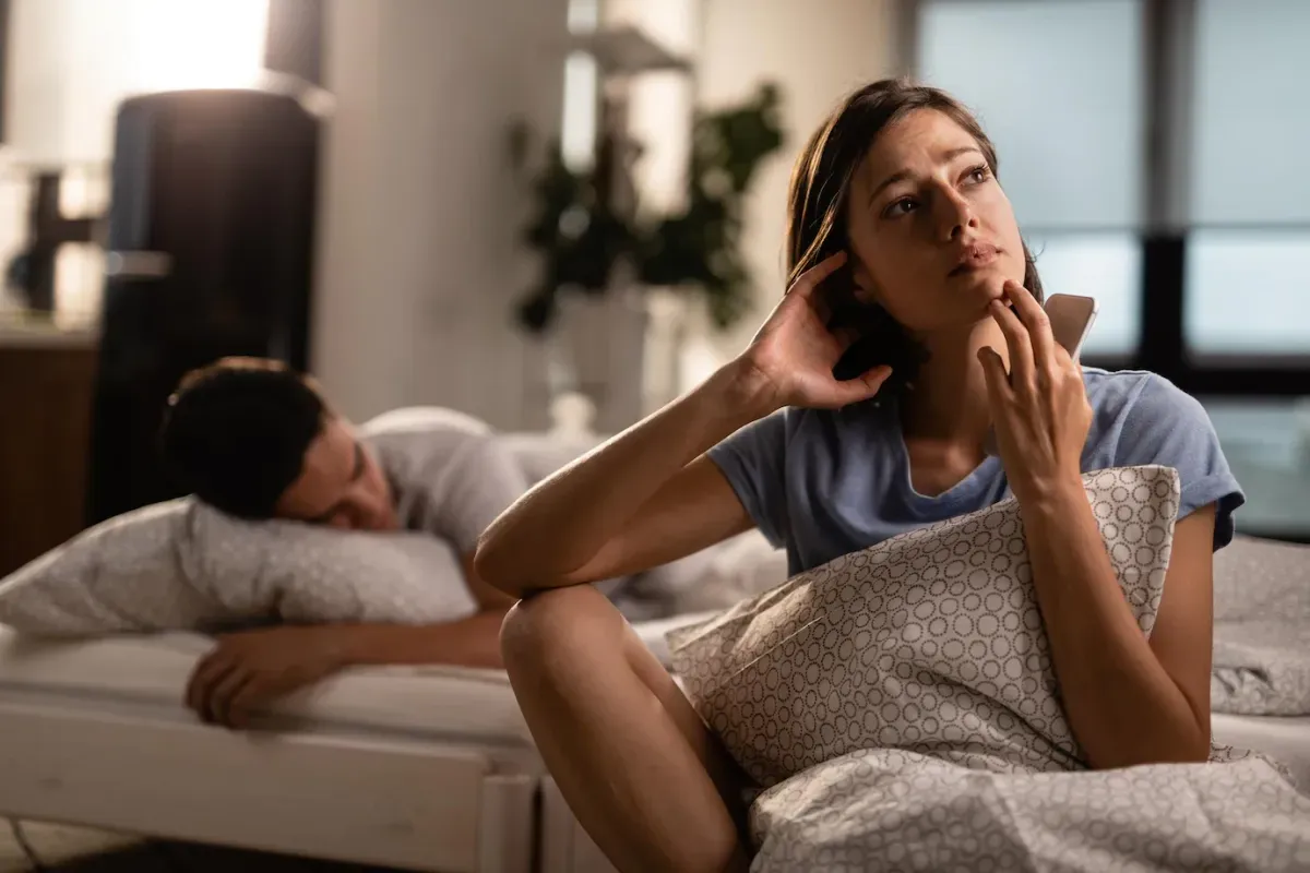 young woman with smart phone contemplating feeling worried about her relationship while boyfriend is sleeping bed 637285 1647 64d0cc99a2446