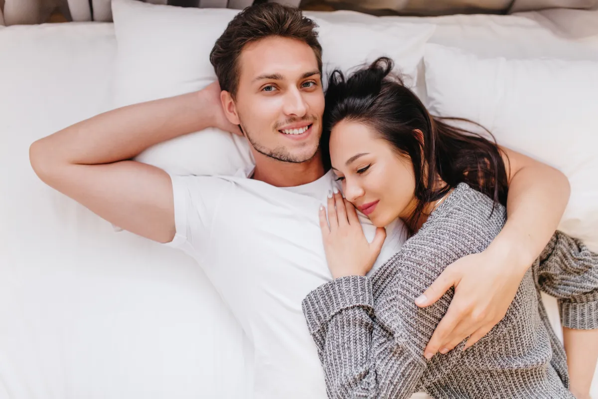 smiling man posing bed with wife sleeping his chest