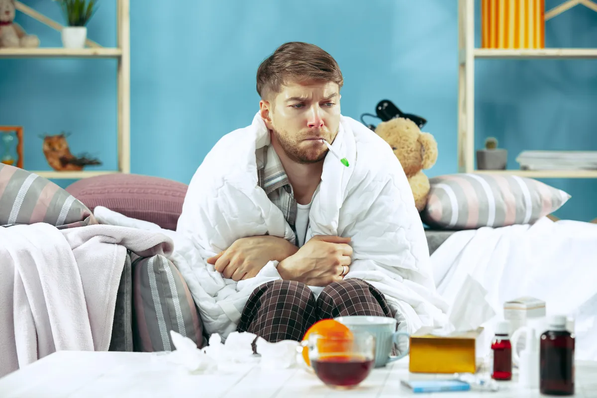 bearded sick man with flue sitting sofa home measuring body temperature winter illness influenza pain concept relaxation home healthcare concepts