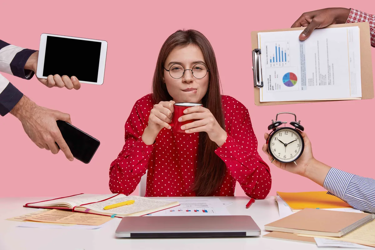 brunette woman sitting desk surrounded with gadgets papers