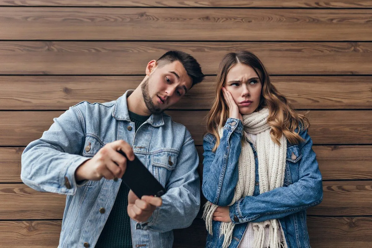 upset charming girl with long scarf looking away while posing wooden wall carefree caucasian man using his smartphone 197531 8362