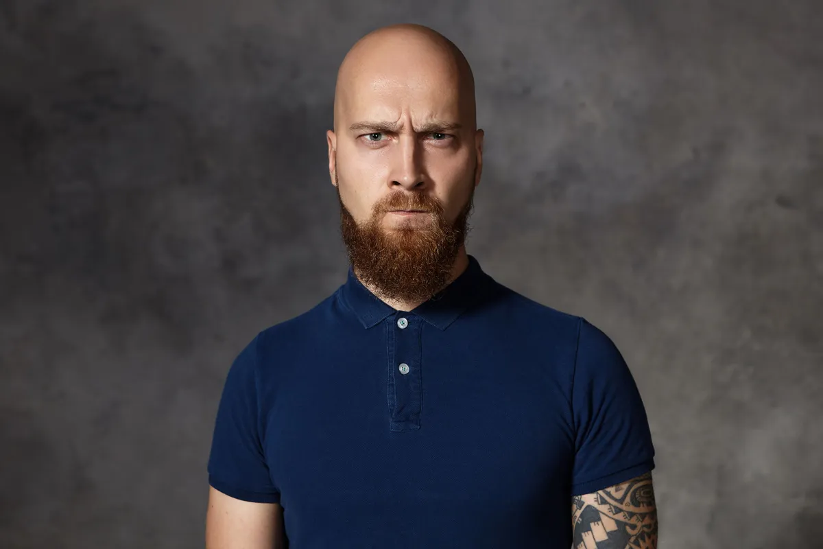 what s your problem picture unfriendly enraged young bearded macho man with shaved head frowning pursuing lips being angry with something his eyes full rage indignation anger