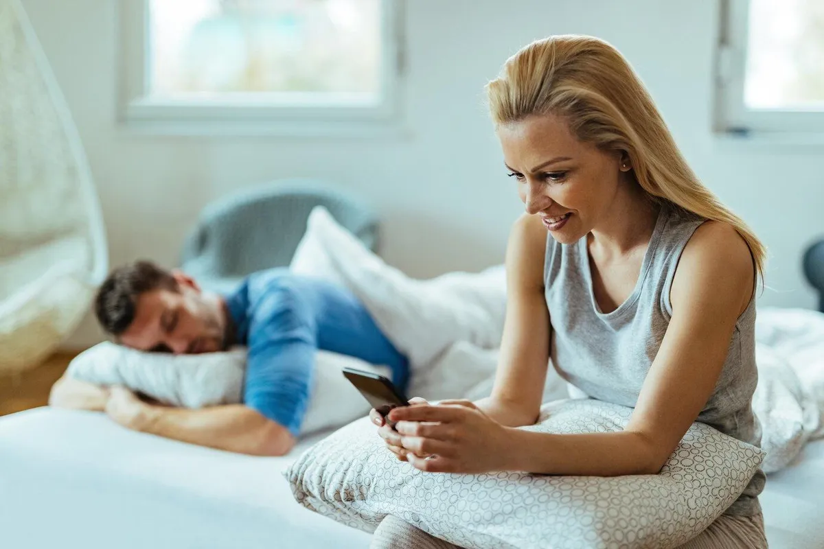 young happy woman using mobile phone while sitting bed her boyfriends is sleeping her 637285 5678