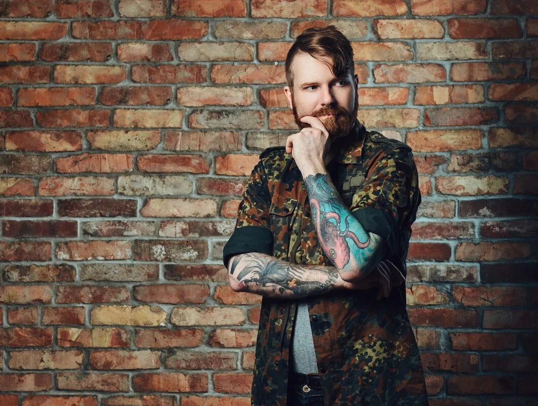 portrait redhead bearded male with tattoos arms dressed military jacket wall brick 613910 3647