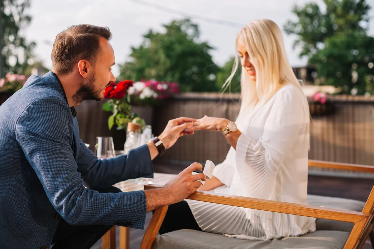 handsome man placing wedding ring blonde woman s hand restaurant