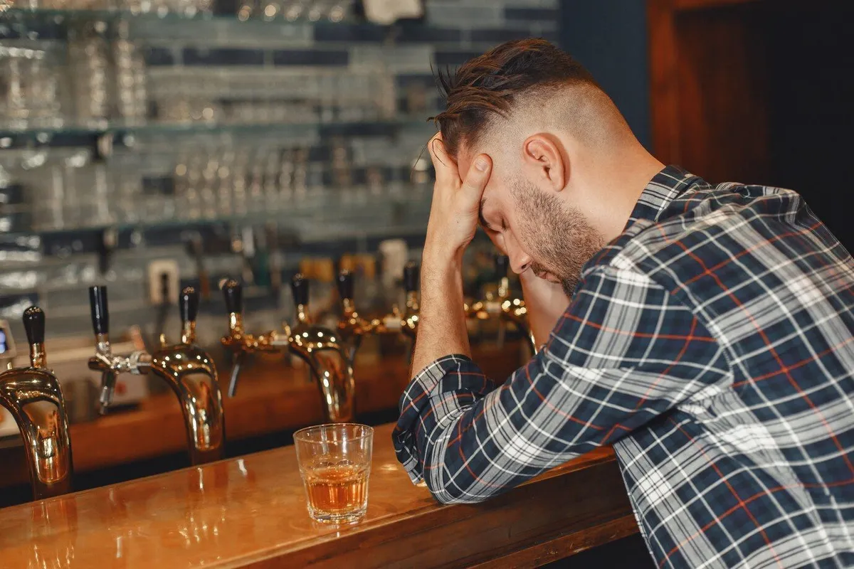 man shirt holds glass his hands guy is sitting bar holding his head 1157 43505