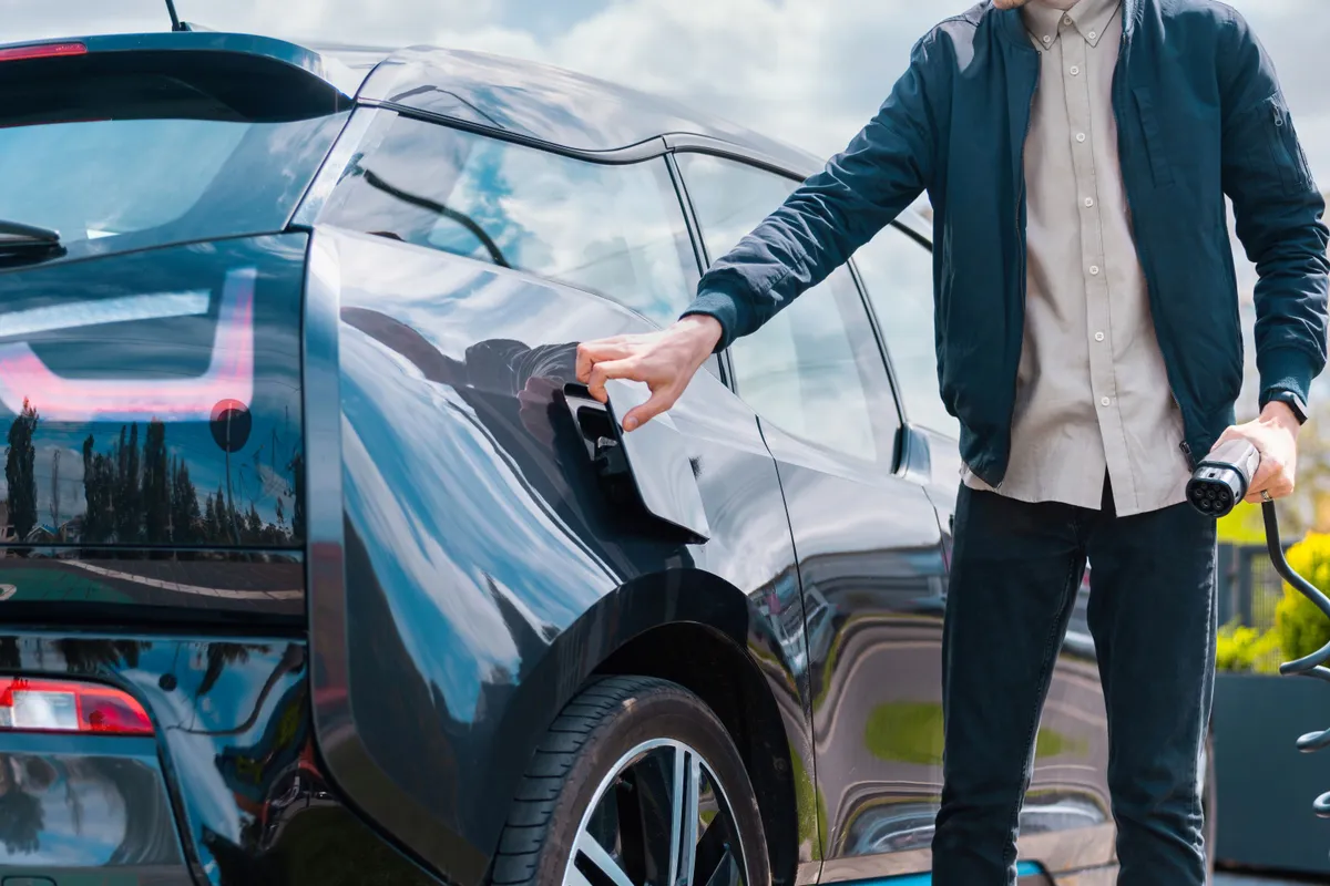man closing cars charge socket holding charger charge station