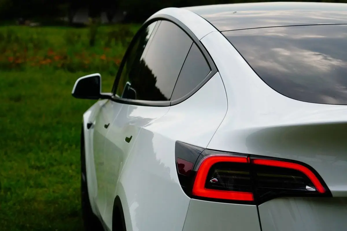 Achterkant van een witte Tesla Model Y met rode achterlichten, geparkeerd naast een grasveld