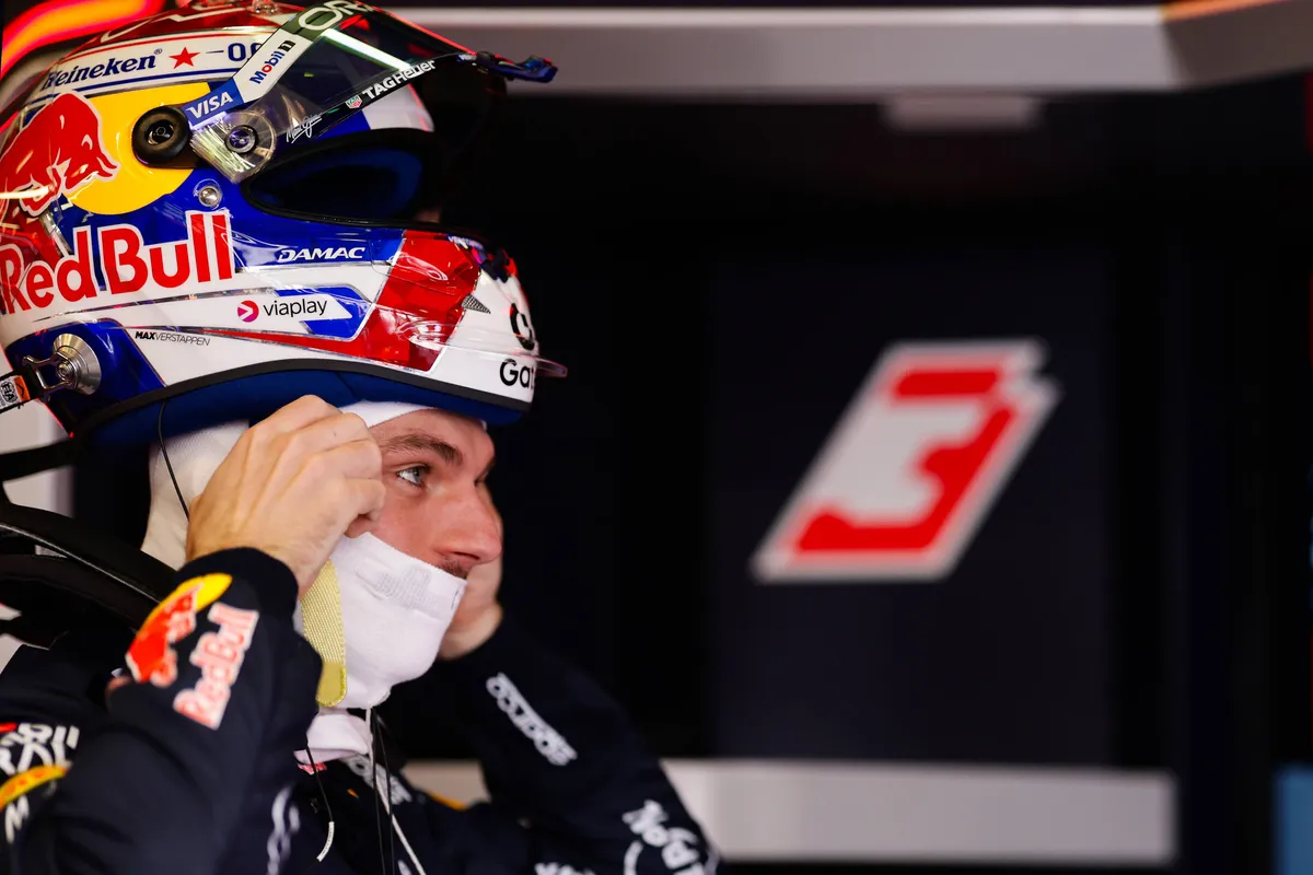 Max Verstappen zet zijn helm op om in het 2026 F1-weekend in Australië de baan op te gaan, met startnummer 3 op de achtergrond in de Red Bull-garage