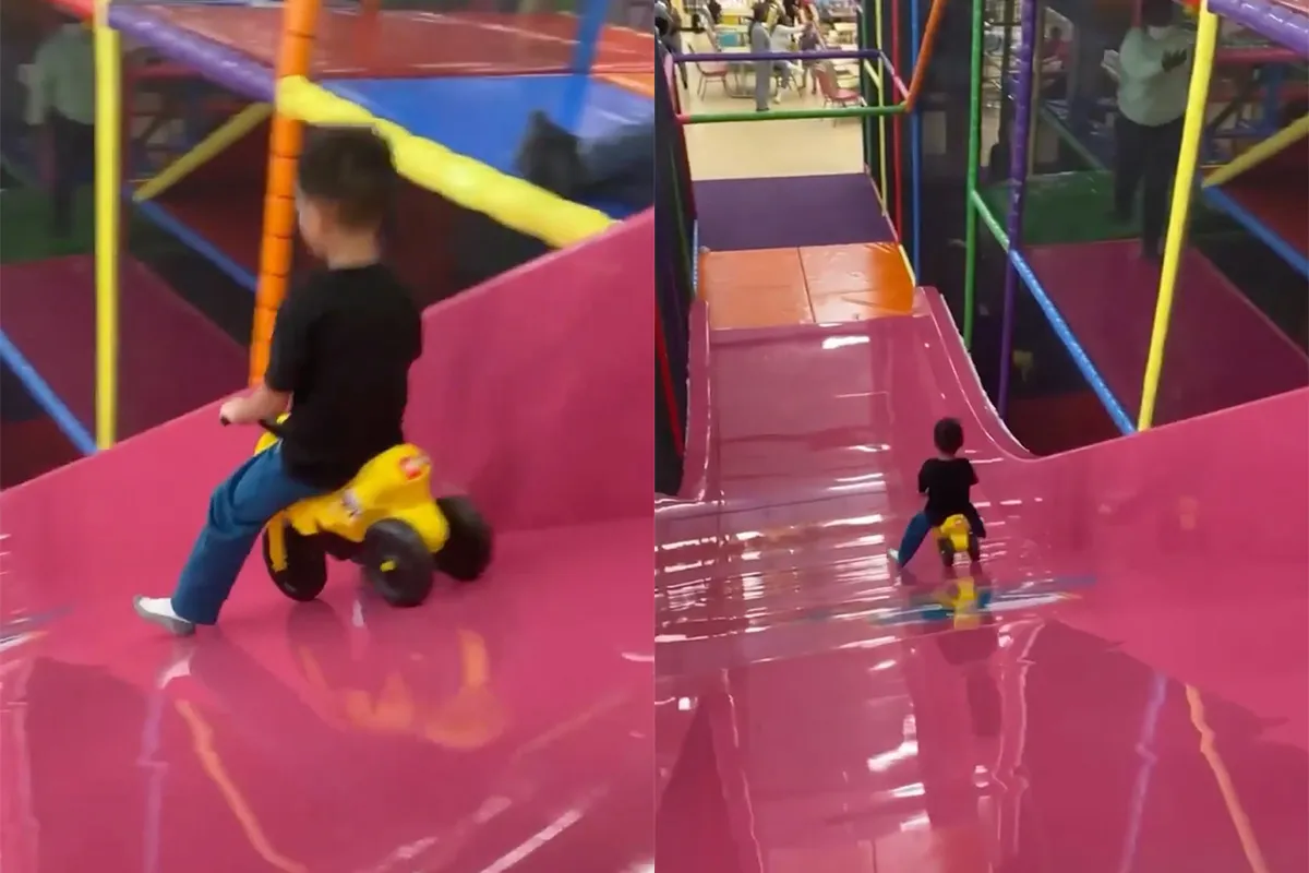 Kleine waaghals gaat met driewieler van glijbaan in binnenspeeltuin