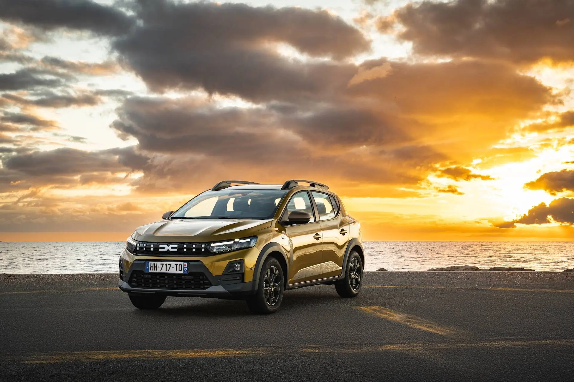 La Dacia Sandero 2026 in versione Stepway fotografata al tramonto davanti al mare in un eliporto, con verniciatura Giallo Ambra