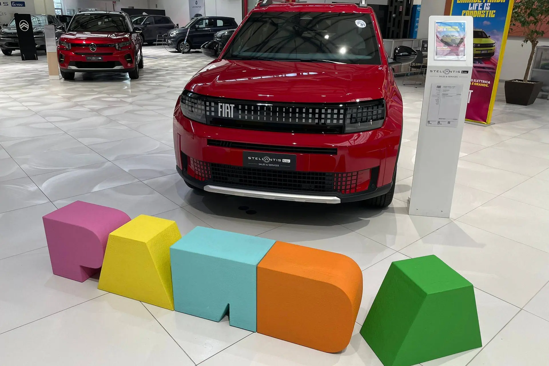 FIAT Grande Panda rossa in salone con scritta panda colorata su sfondo pavimento bianco