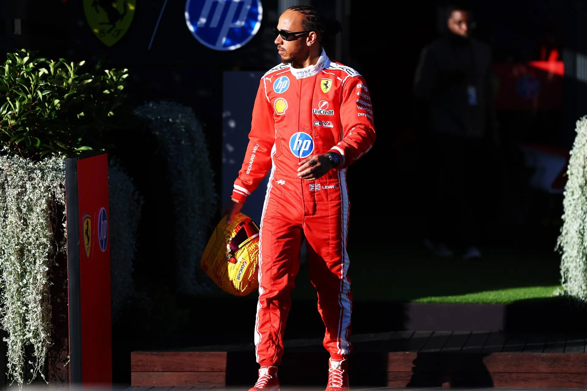 lewis hamilton pilota ferrari che cammina con la tuta rossa e il casco lego giallo