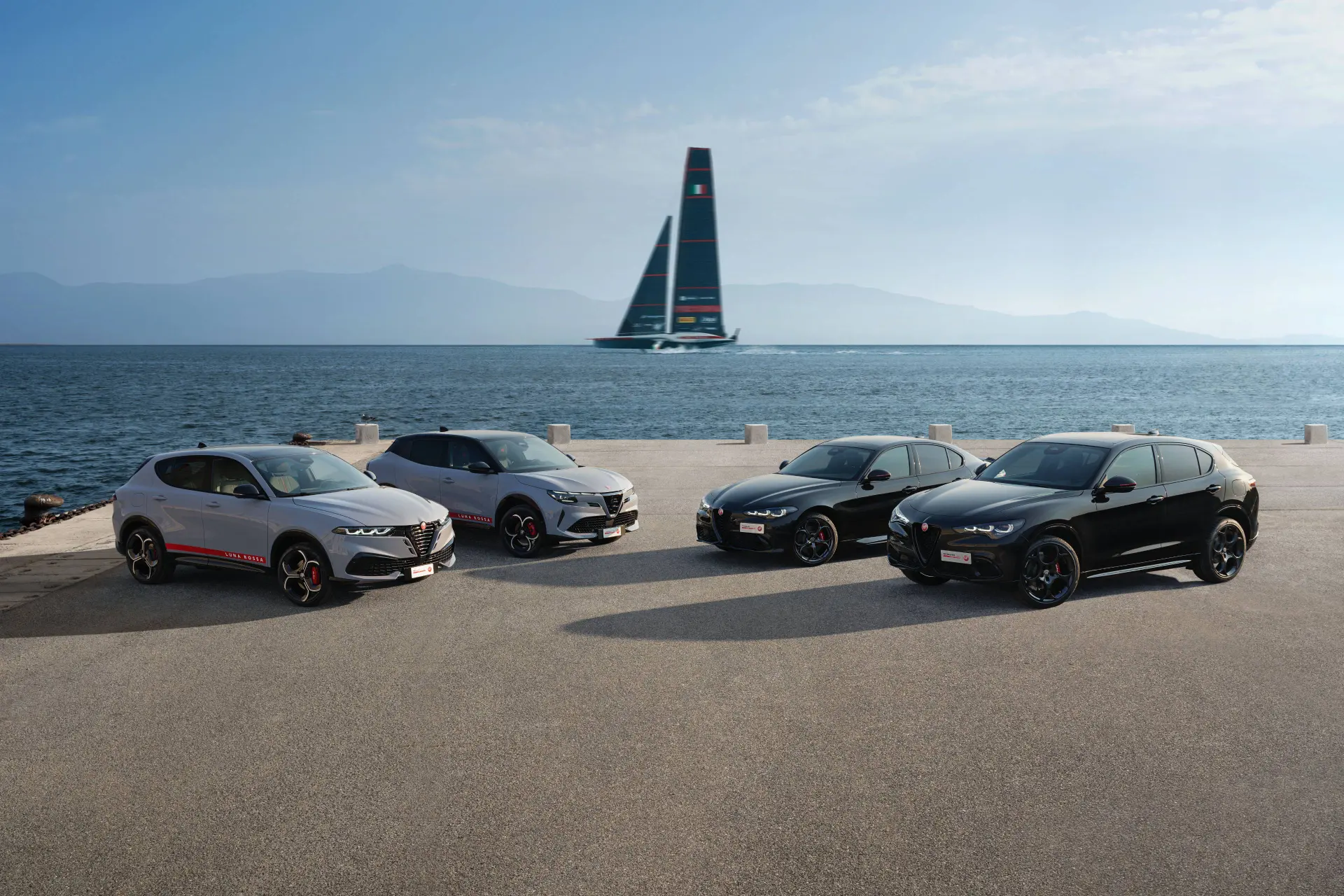 Nell'immagine si vede la gamma di Alfa Romeo in collaborazione con Luna Rossa. Sullo sfondo si vede una delle vele da gara di Luna Rossa