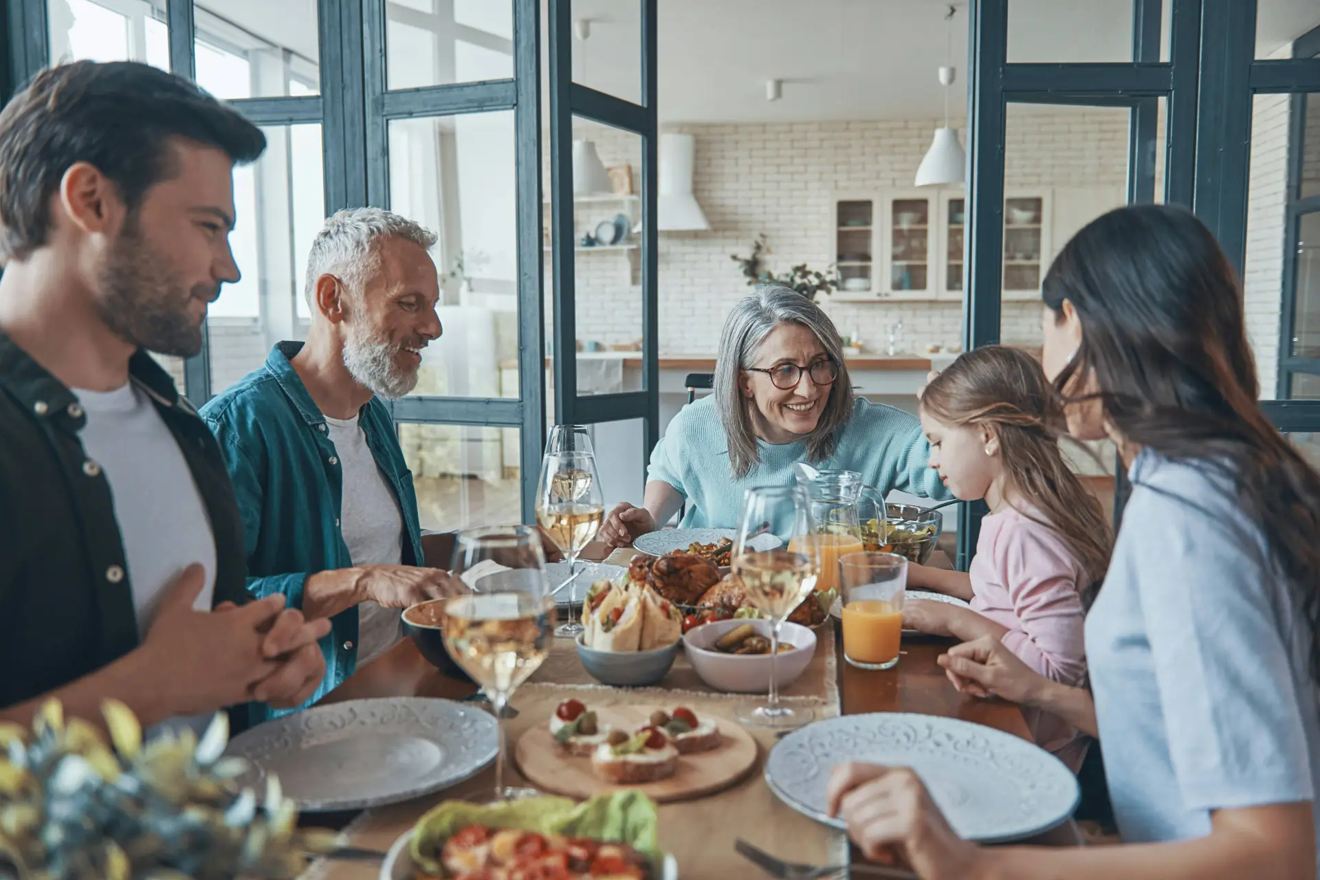 A multi-generational family enjoys a meal together around a dining table filled with food and drinks.