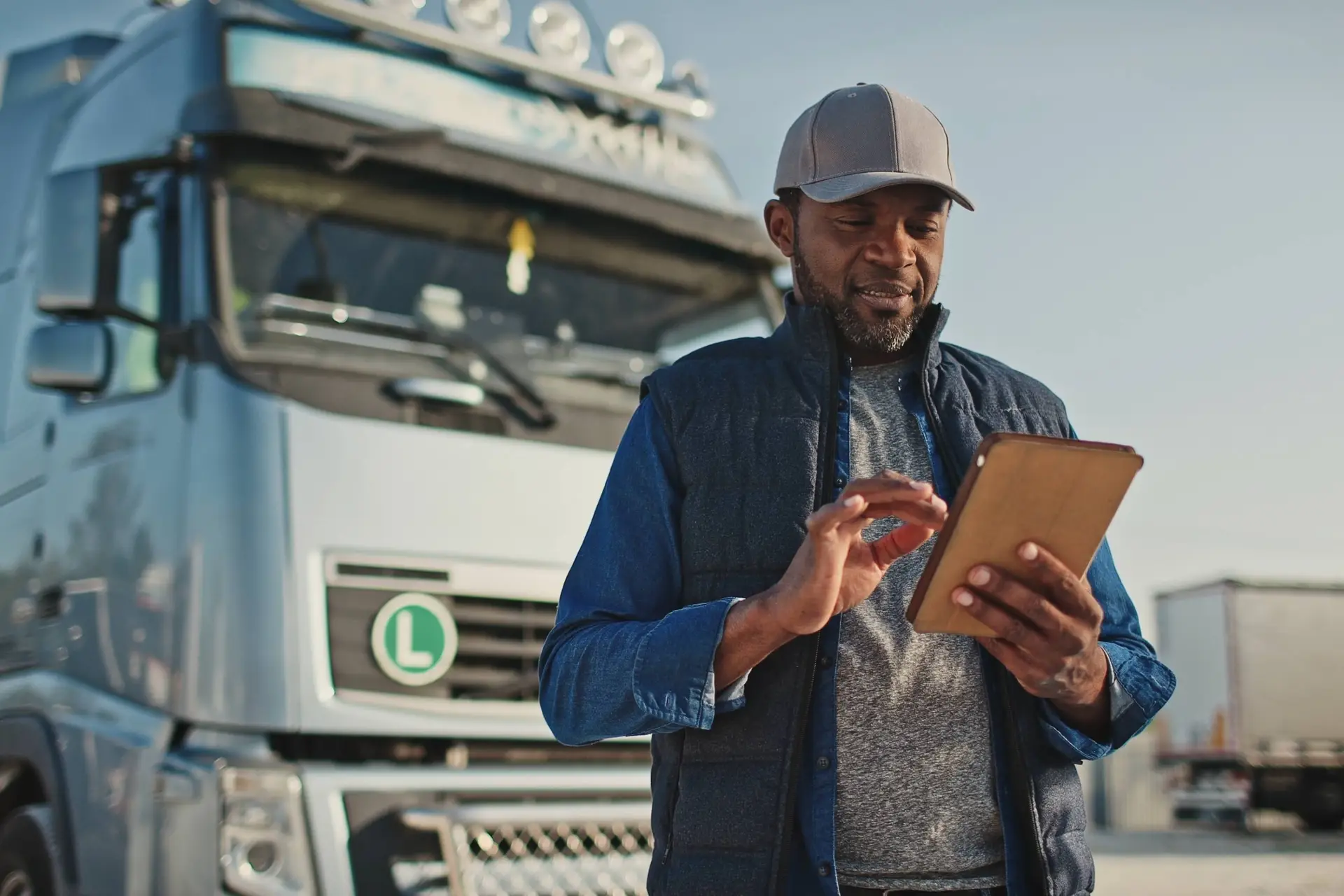 Vrachtwagenchauffeur met pet bekijkt een tablet naast zijn vrachtwagen