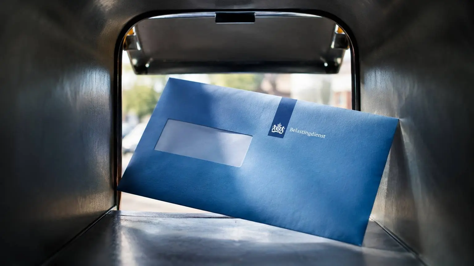 Blauwe envelop van de Belastingdienst bij een brievenbus.