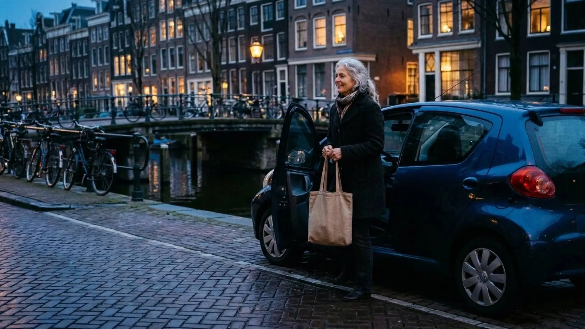 Vrouw van rond de zestig met boodschappentas stapt in de schemering uit haar auto langs een Amsterdamse gracht
