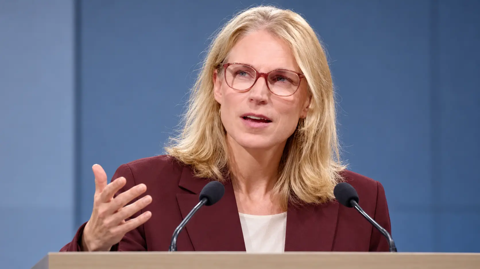 Illustratie van minister Elanor Boekholt-O’Sullivan achter een spreekgestoelte, na haar akkoord over extra woonruimte voor statushouders