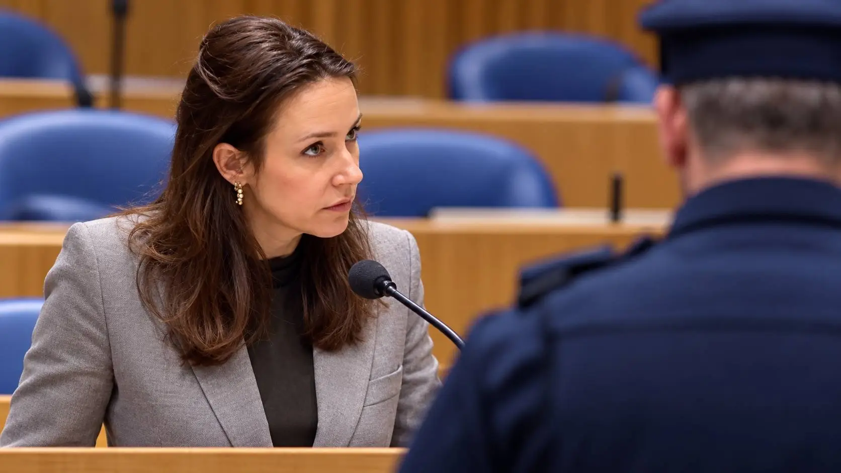 AI-illustratie van Claire Martens-America in de Tweede Kamer, met op de voorgrond een boa van achteren in neutraal uniform.