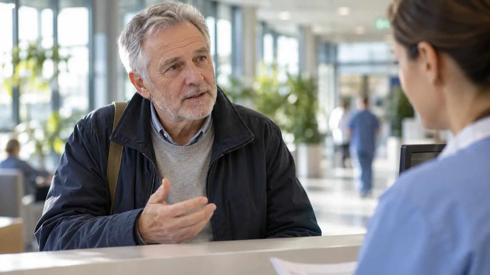 Man van rond de zestig in gesprek met een medewerker bij de inschrijfbalie van een ziekenhuis