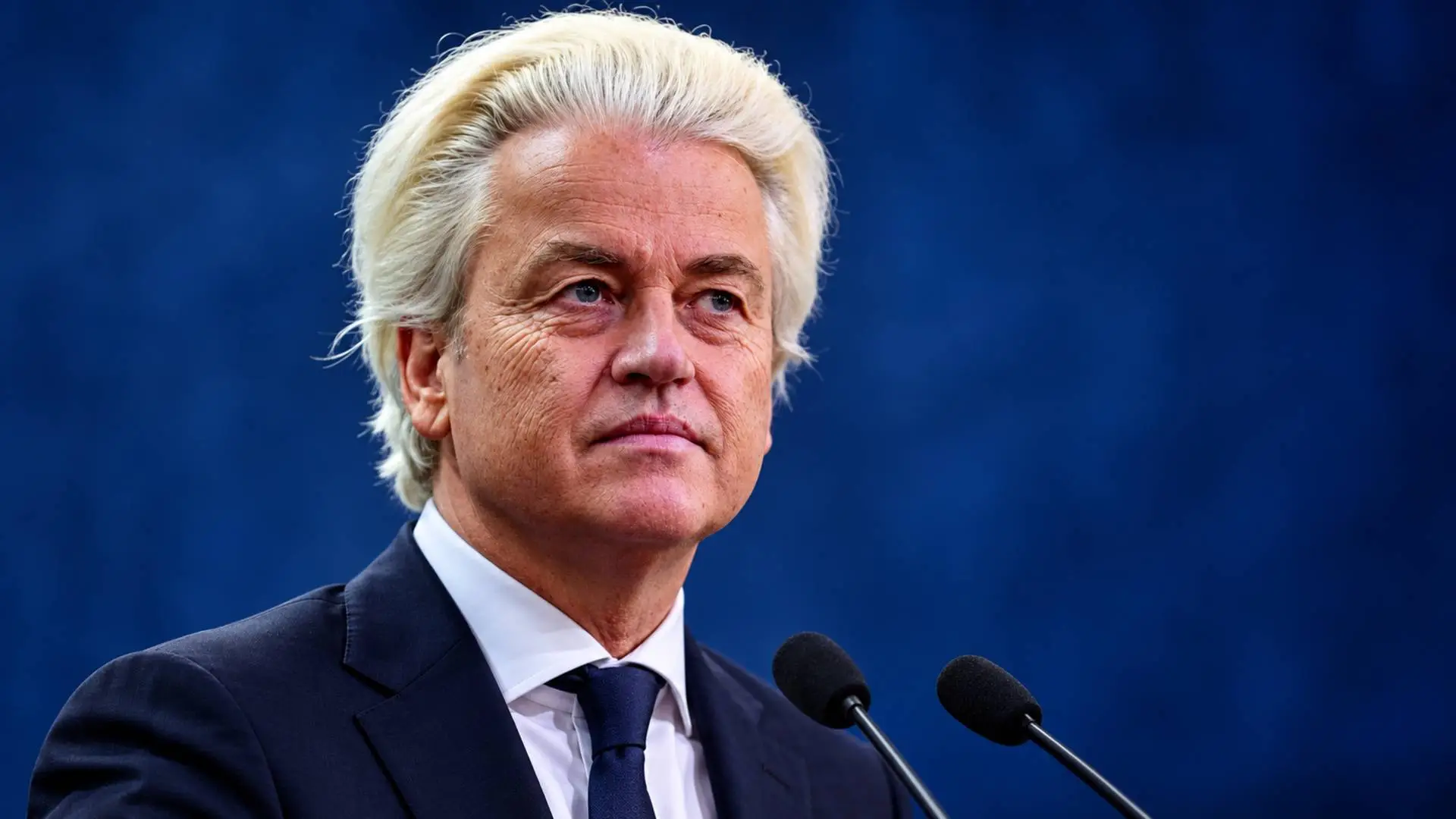 Portretillustratie van Geert Wilders achter twee microfoons tegen een donkerblauwe achtergrond.