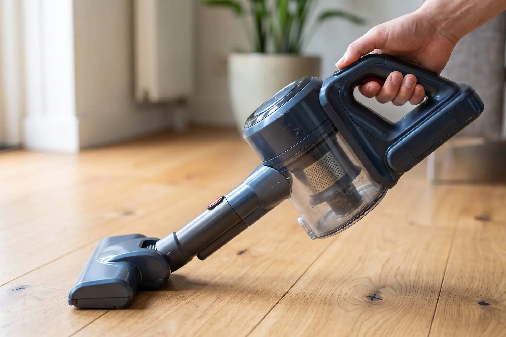 Een hand die de aan-knop van een draadloze stofzuiger indrukt.
