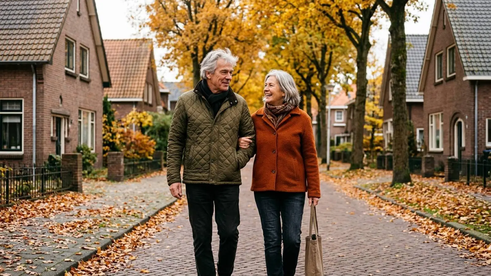 Een Nederlands echtpaar van begin zestig wandelt in de herfst langs een rij bakstenen woningen.