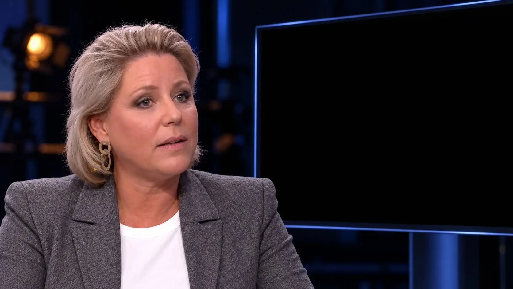 AI-illustratie van Rianne Letschert in een donkere studio naast een volledig zwart televisiescherm