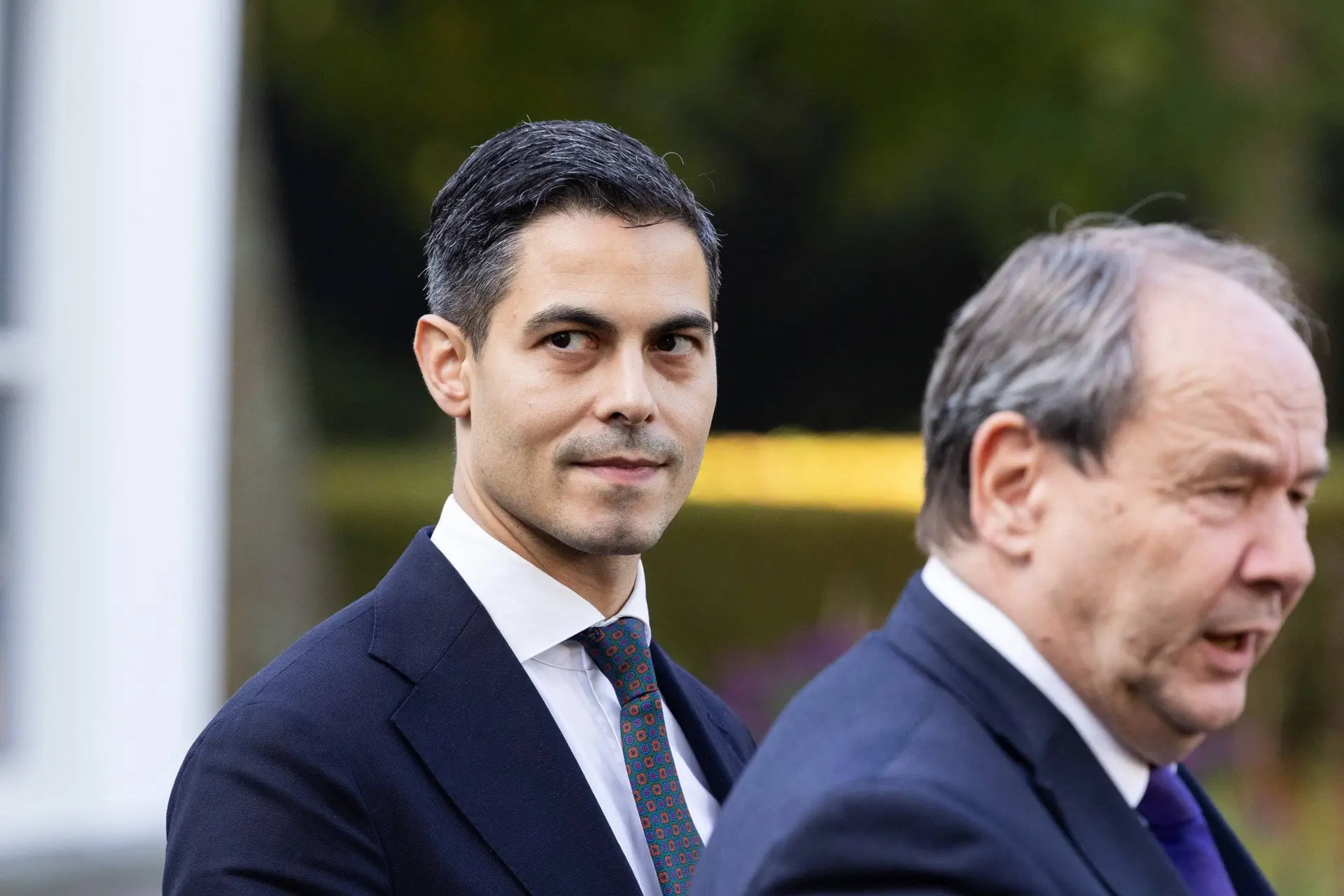 Premier Rob Jetten kijkt opzij terwijl een man naast hem praat; Jetten haalde de WW- en WIA-ingrepen van tafel