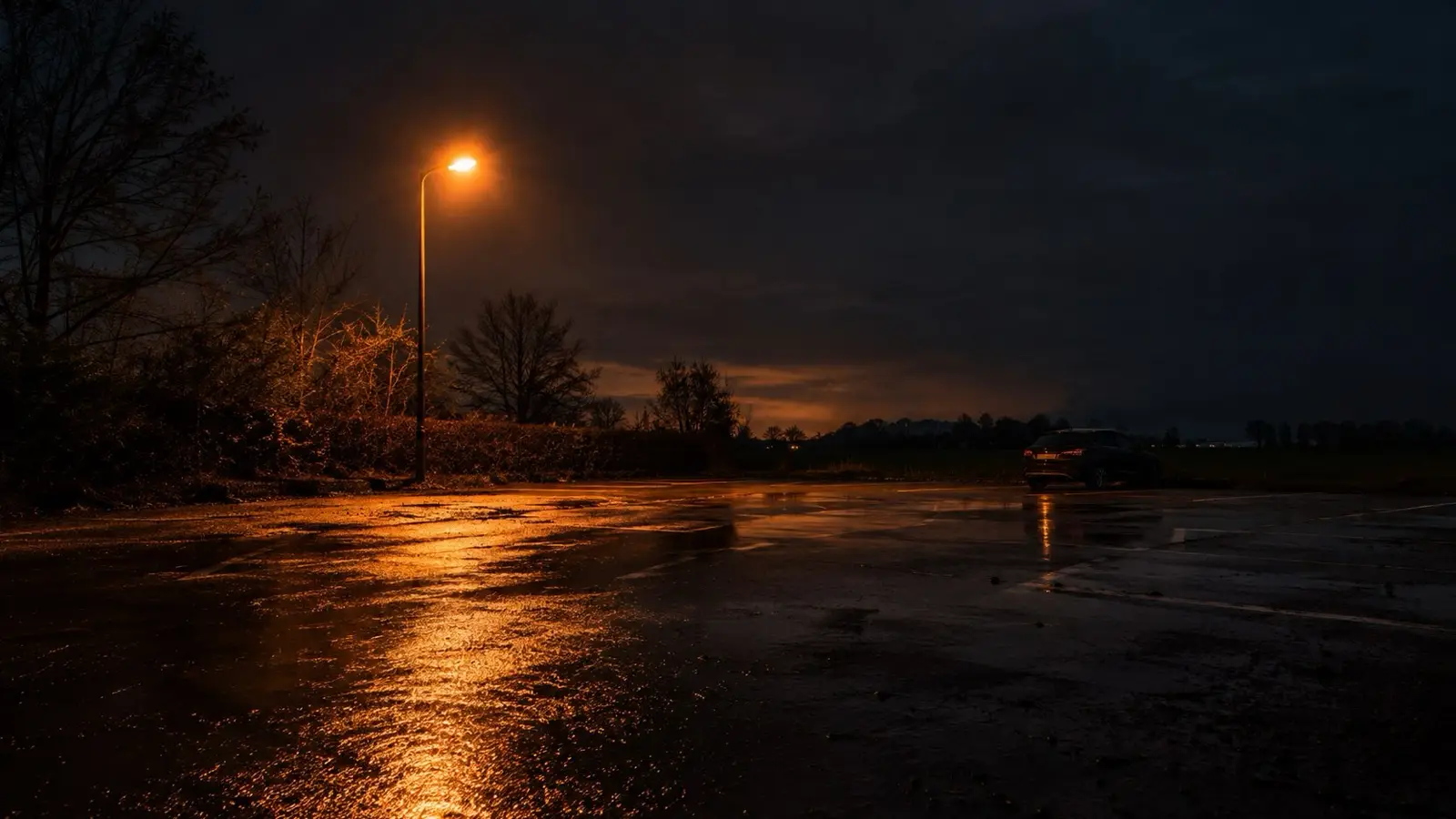Verlaten natte parkeerplaats bij avond onder een oranje lantaarnpaal