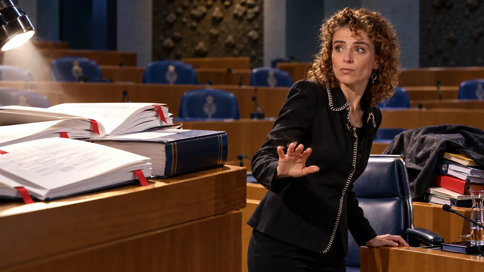 Illustratie van Sophie Hermans. Illustratie van opengeslagen onderzoeksrapporten en een wetboek op een parlementair spreekgestoelte tegenover een lege ministeriële stoel met weggemoffelde dossiers.