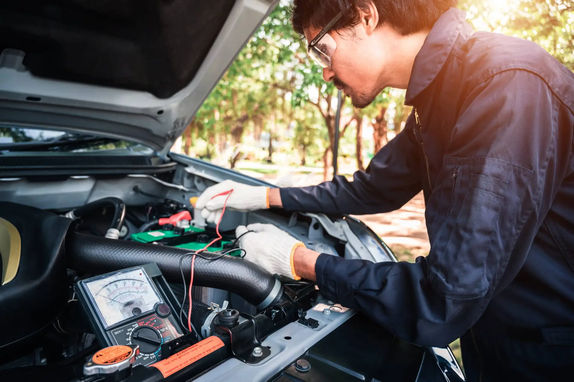 Een monteur meet met een accutester de spanning van een auto-accu onder de geopende motorkap.