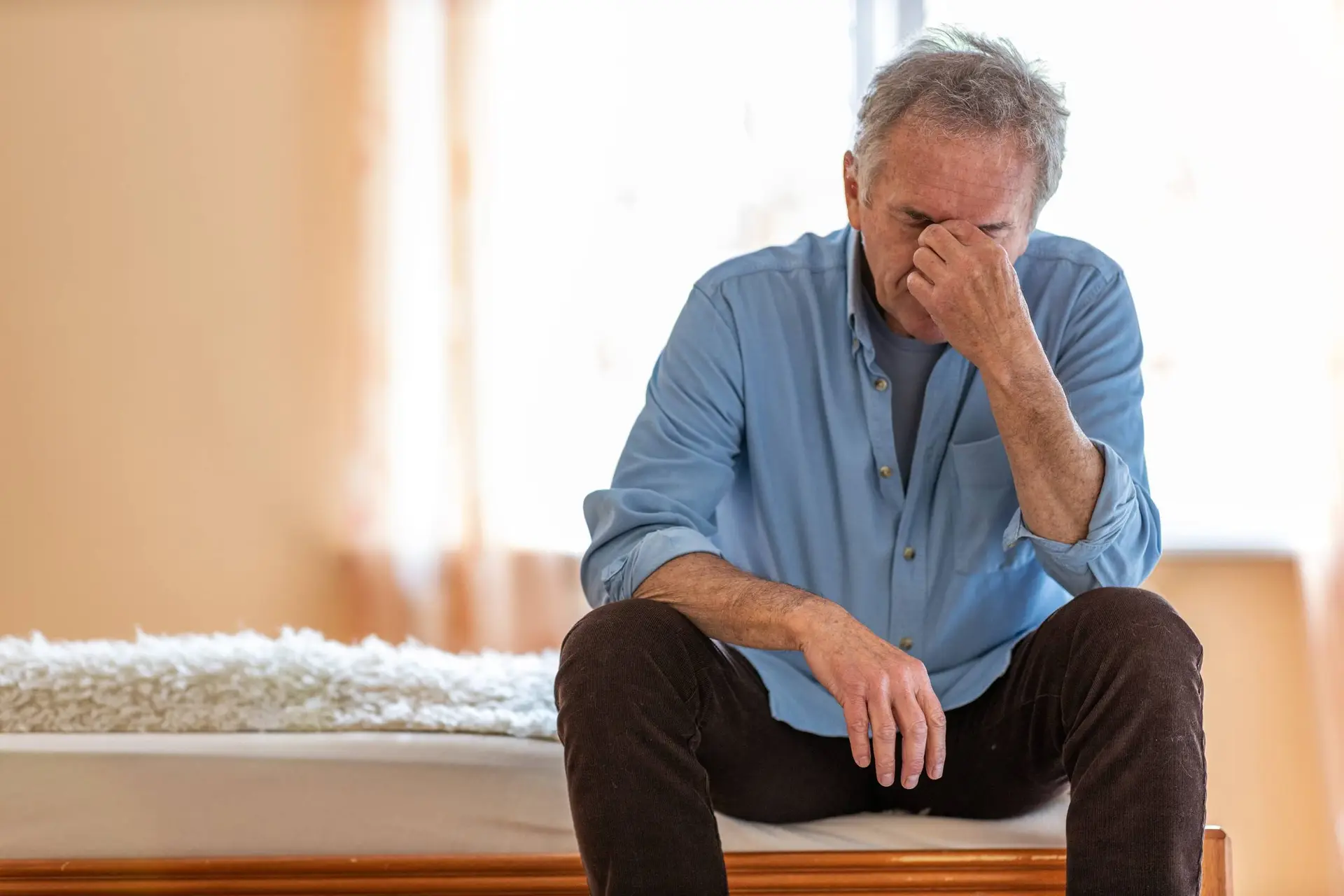 Een man van middelbare leeftijd zit ’s ochtends vermoeid op de rand van zijn bed.