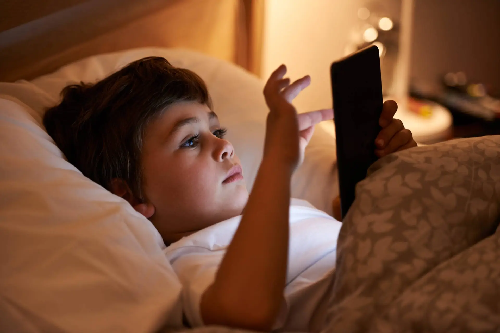Een tiener ligt ’s avonds in bed en kijkt op het verlichte scherm van een smartphone.