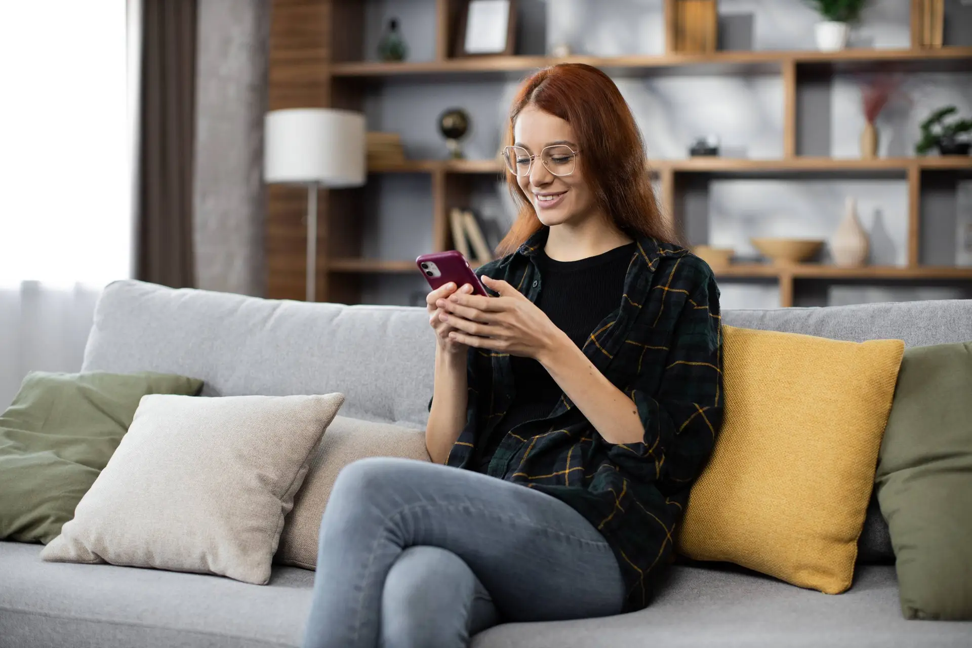 Een vrouw zit op de bank en typt op haar telefoon een tekst voor haar datingprofiel.