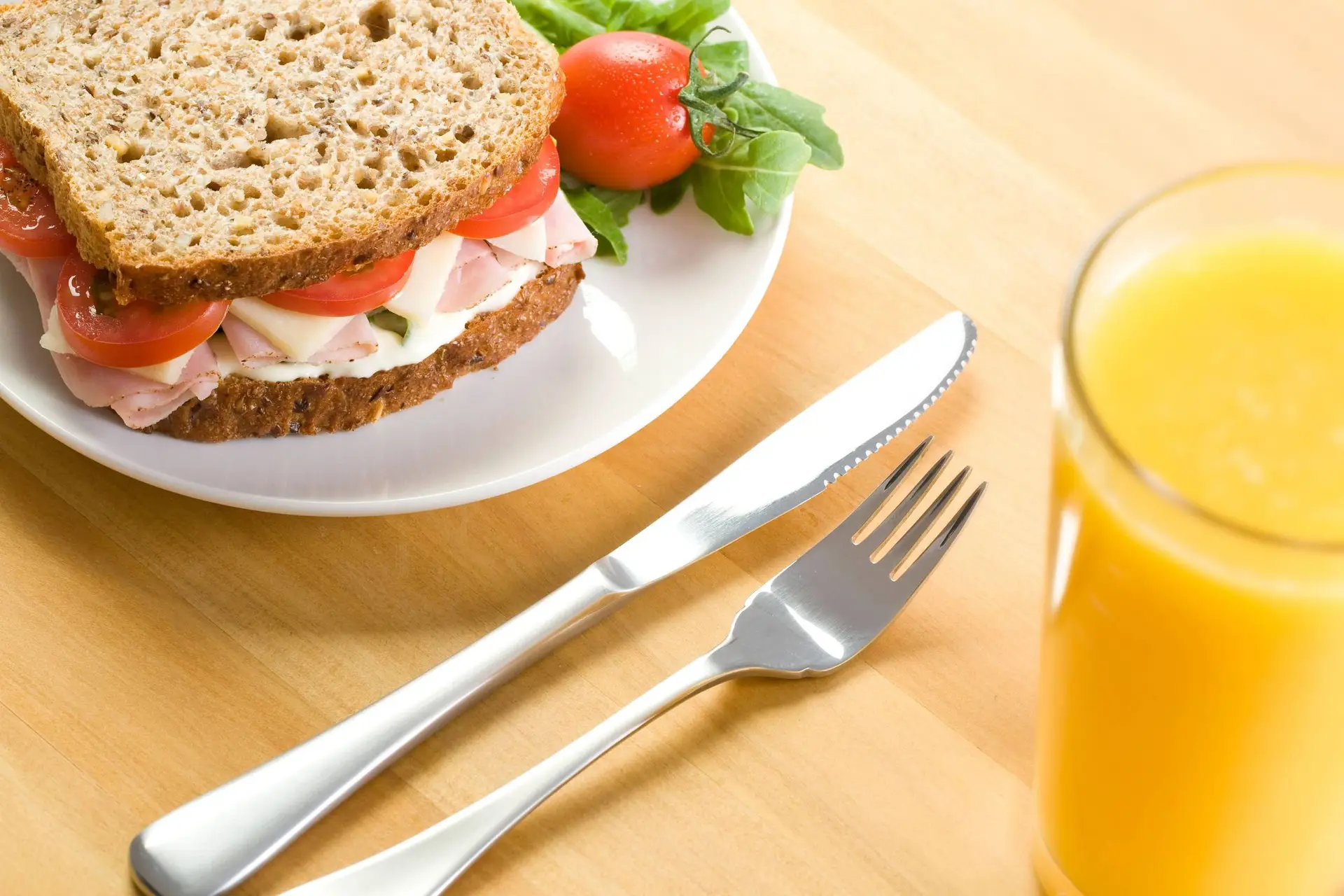 Gezonde ham, kaas, tomaat en raket volkoren sandwich met een vers glas sap.