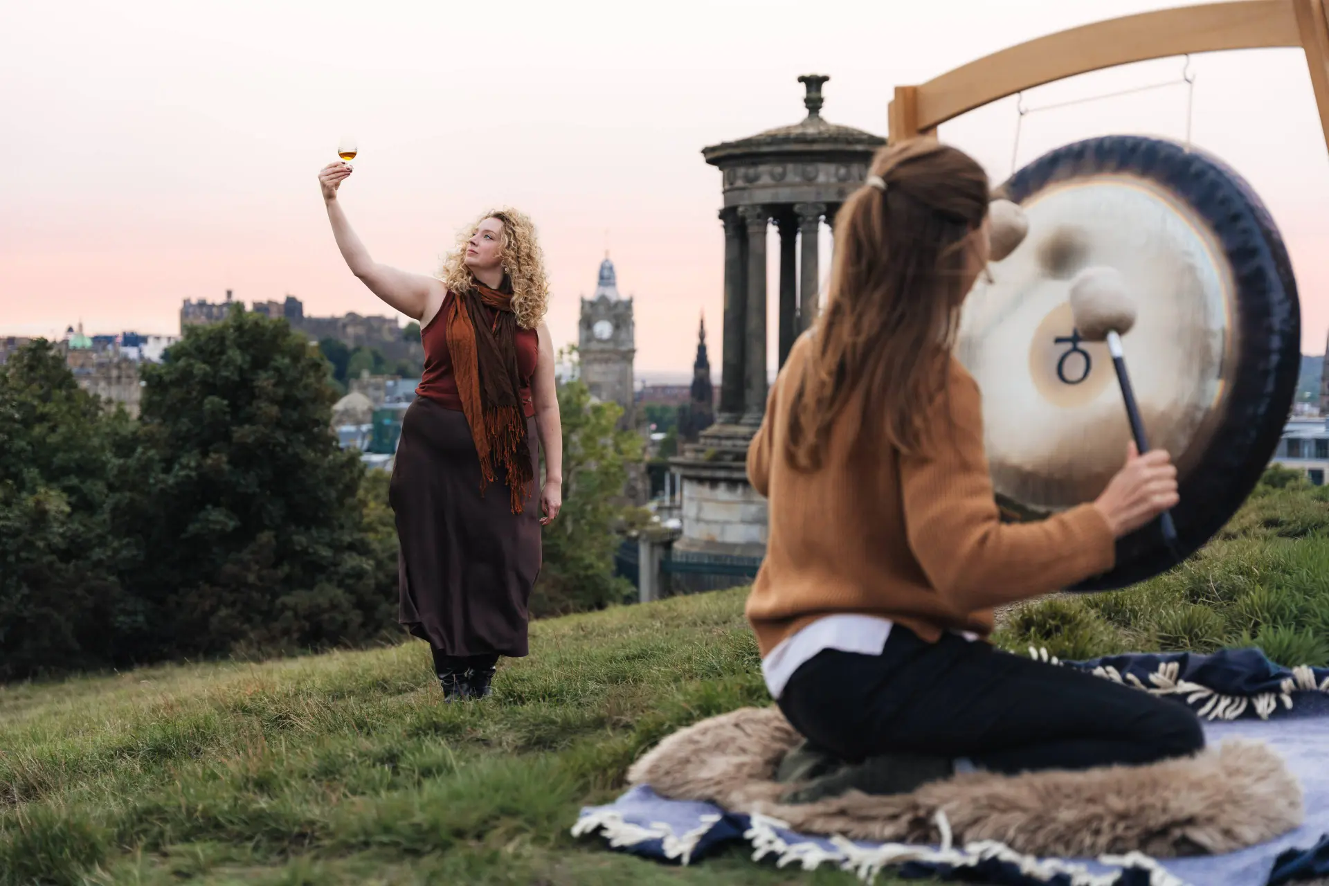 Madeleine Schmoll of The Scotch Malt Whisky Society raises a dram to toast the start of whisky season on Calton Hill, Edinburgh, with Jo McCoy of Blissness, a gong sound bath practitioner