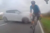 Engelse wielrenner heeft engeltje op zijn schouder, wordt bijna gegrepen door langs vliegende auto
