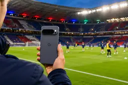 Google Pixel-smartphone op de voorgrond in een voetbalstadion tijdens de warming-up van spelers op het veld.